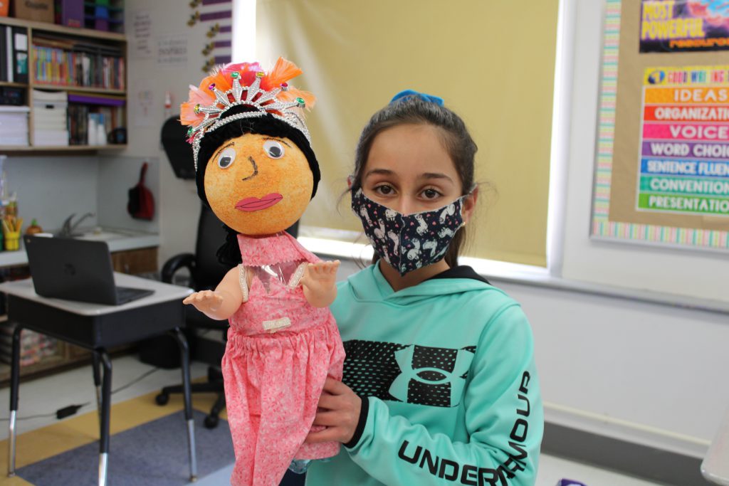 student with a dark haired ponytail and wearing a mask holds up a 3d model of a ballerina made out of a soda bottle