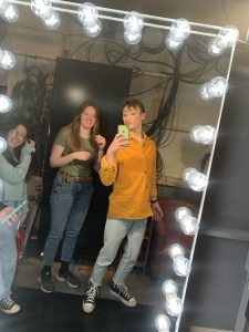 a boy wearing a yellow shirt takes a selfie photo in a lighted mirror