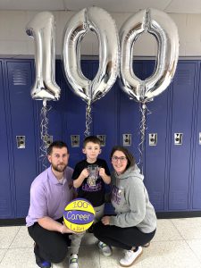a young couple pose with a child holding a basketball and balloons that read 100