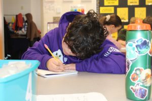 a young boy wearing a purple sweatshirt writes into a notebook
