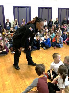 a police officer leans over to talk to students at an assembly