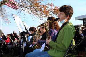 a young boy wearing a green shirt plays a saxophone outside as part of a band