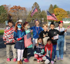 a group of school children holding American flags pose together outside