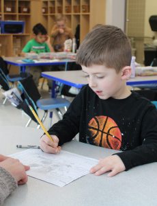 a young boy wearing a t-shirt with a basketball on it writes on a piece of paper