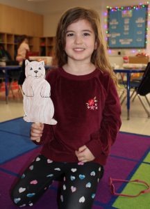 a young girl with dark hair holds up a drawing of a groundhog