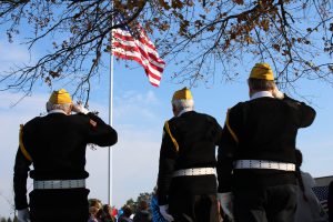 three elderly veterans wearing black clothes and yellow hats pay tribute to an American flag
