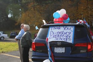 two male veterans stand outside their car which is decorated with red, white and blue balloons and a sign that says "Thank you Duanesburg Elementary School"