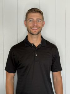 a young man with a dark shirt poses in front of a white wall