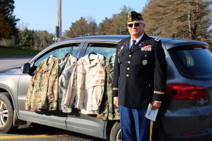 a man dressed in military uniform poses outside of his car, which displays various camouflaged tops
