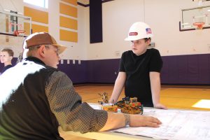 a young boy wearing a hard hat talks to an adult
