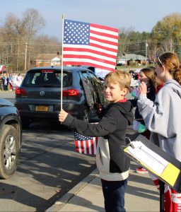 a boy waves an American flag at veterans who drive by in their cars