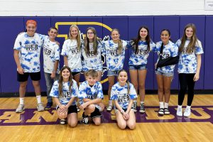 a group of young students pose in a gymnasium wearing tie-dyed shirts