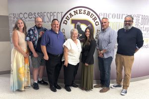 seven adults pose in the hallway in front of a school logo
