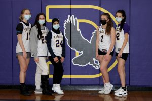 Five female athletes pose in front of their school logo, an eagle, inside a gymnasium