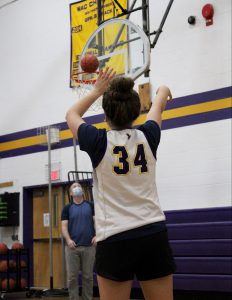 a young female athlete wearing a white jersey shoots a basketball inside a gymnasium