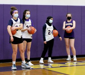 four basketball players await instructions from their coach during a practice session inside a gymnasium