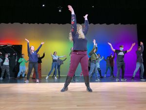 a woman shows choreography to students on a stage