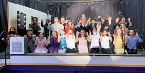 the cast of an elementary school pay pose on stage