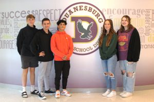 five teenaged students stand in a hallway around their school logo
