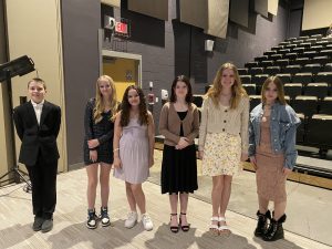 five female students and one male student stand on a theatrical stage