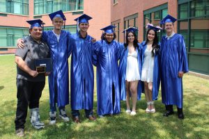 graduates wearing blue caps and gowns pose outside a school