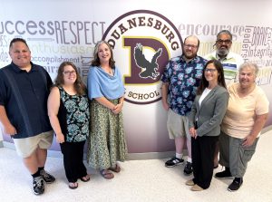 a group of adults pose in front of a school logo in the hallway