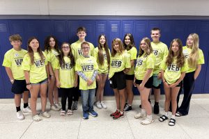 teenagers wearing yellow t-shirts pose in front of purple lockers.