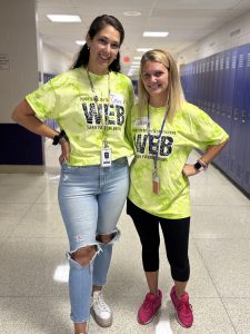 two adult women wearing yellow t-shirts pose in a school hallway