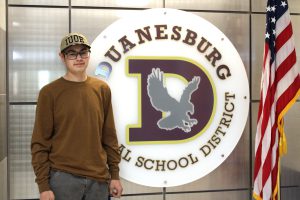 a young man stands next to the Duanesburg school logo