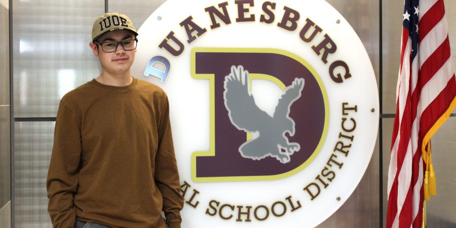 a young man stands next to the Duanesburg school logo