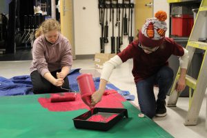 two students use red paint to decorate theater scenery