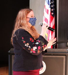 a woman speaks into a microphone on a theatrical stage