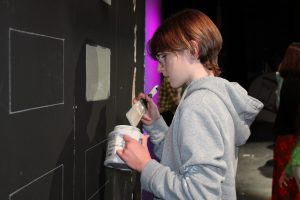 a student paints scenery on a theatrical stage