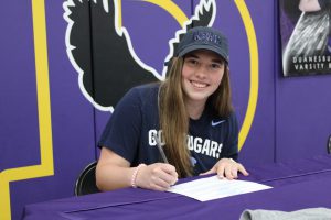 a girl wearing a blue hat signs a piece of paper