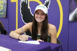 a girl wearing a white hat signs a piece of paper