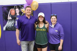 a man poses with two women in a gymnasium