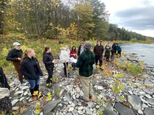 a group of teen science students participate in an experiment on the shoreline of a creek
