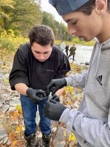two teen male students test water quality on the banks of a river 