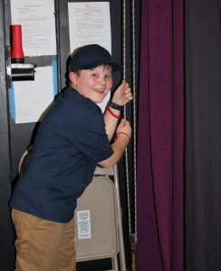 a young boy pulls a stage curtain shut