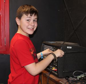 a young man turns knobs on a piece of technical equipment backstage at a play