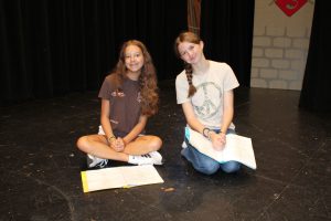 two female students pose on the stage during rehearsal