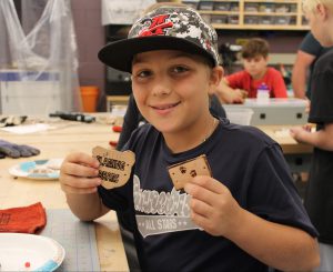 a boy with a hat shows off a leather piece of art that he created
