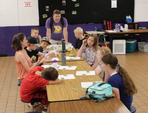 students and two teachers sit at a table to learn a science lesson