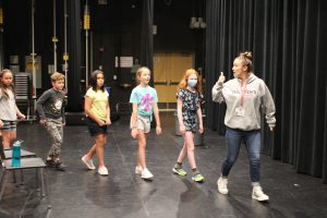 an adult actor leads a line of youth actors on a stage