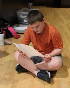 a young student sits on a stage and practices lines for a play