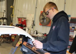 a young man with a blue hoodie works on a car