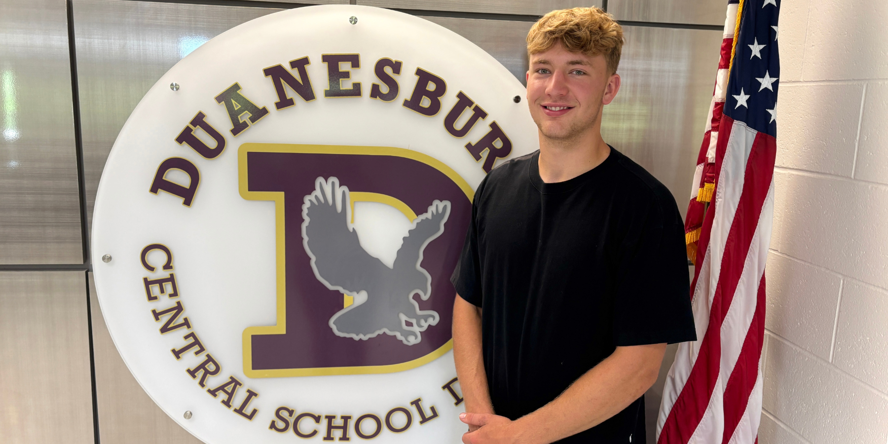 a young man poses in front of a school logo
