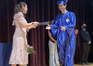 a young man wearing a blue cap and gown receives a diploma