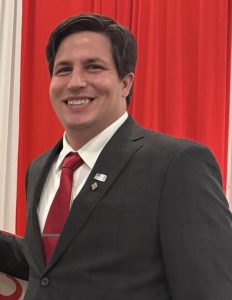 a man wearing a suit and tie stands in front of a red curtain