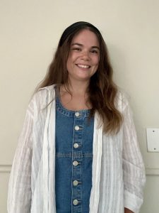 a woman with long brown hair wears a denim dress with a white coat over it